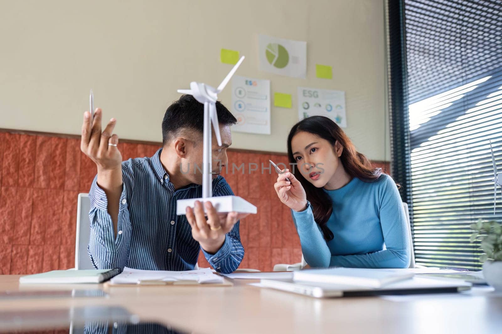 Two professionals brainstorm ESG initiatives while examining a wind turbine model, focusing on sustainable practices.