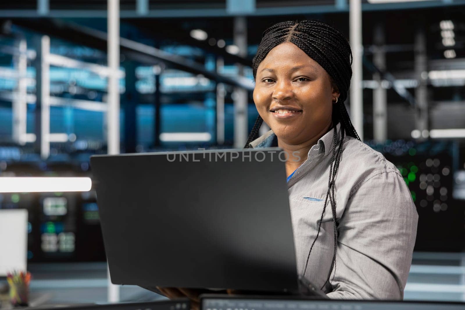 Portrait of smiling data center software developer using artificial intelligence neural networks. Cheerful server farm worker uses AI programming language on computer, configuring specialized hardware