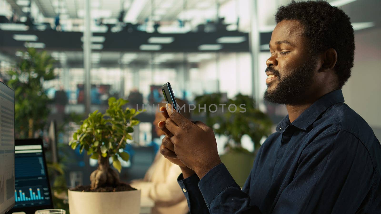 Employee in office taking break from checking documents to text friends using smartphone, relaxing. Accountant in office pausing tasks to answer messages on mobile phone, camera B
