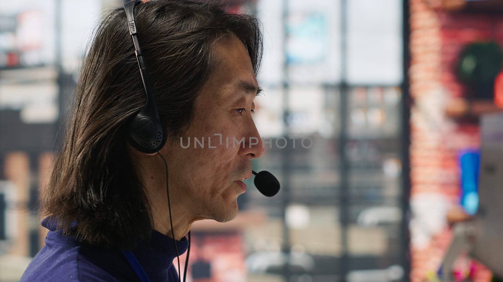 Closeup of senior call center agent helping customers regain access to accounts, resetting passwords. Experienced Asian worker in diverse customer center assisting clients needing help, camera A