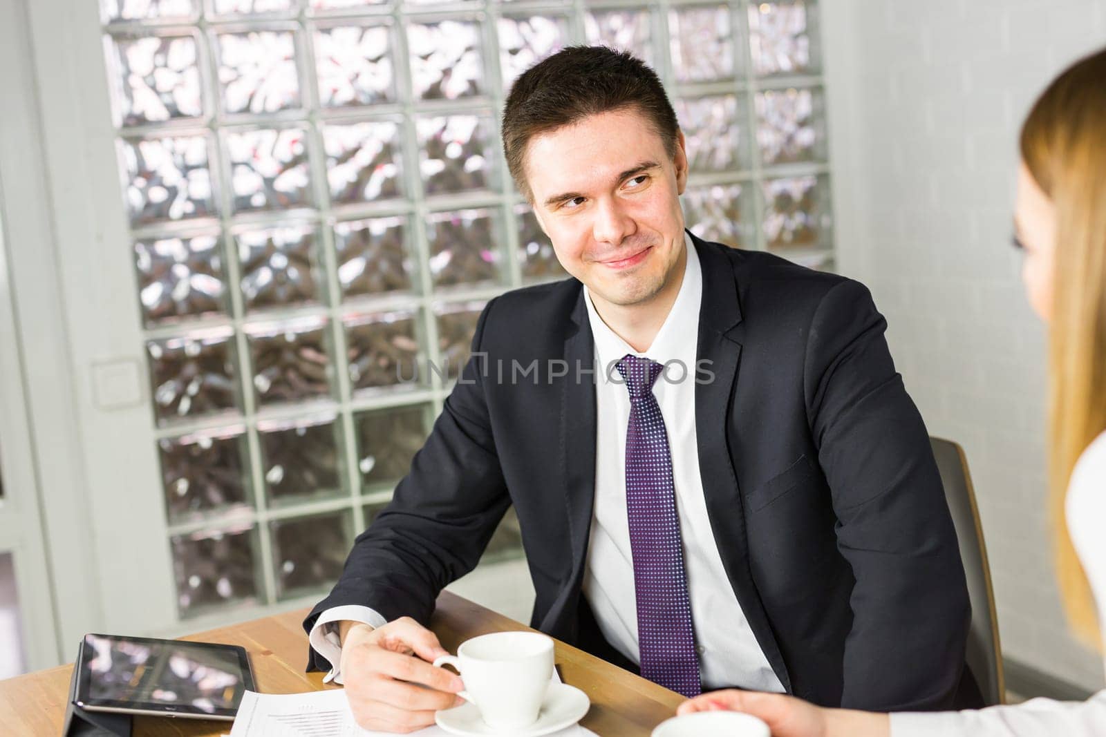 Office coffee break with two colleagues sitting chatting over cups.