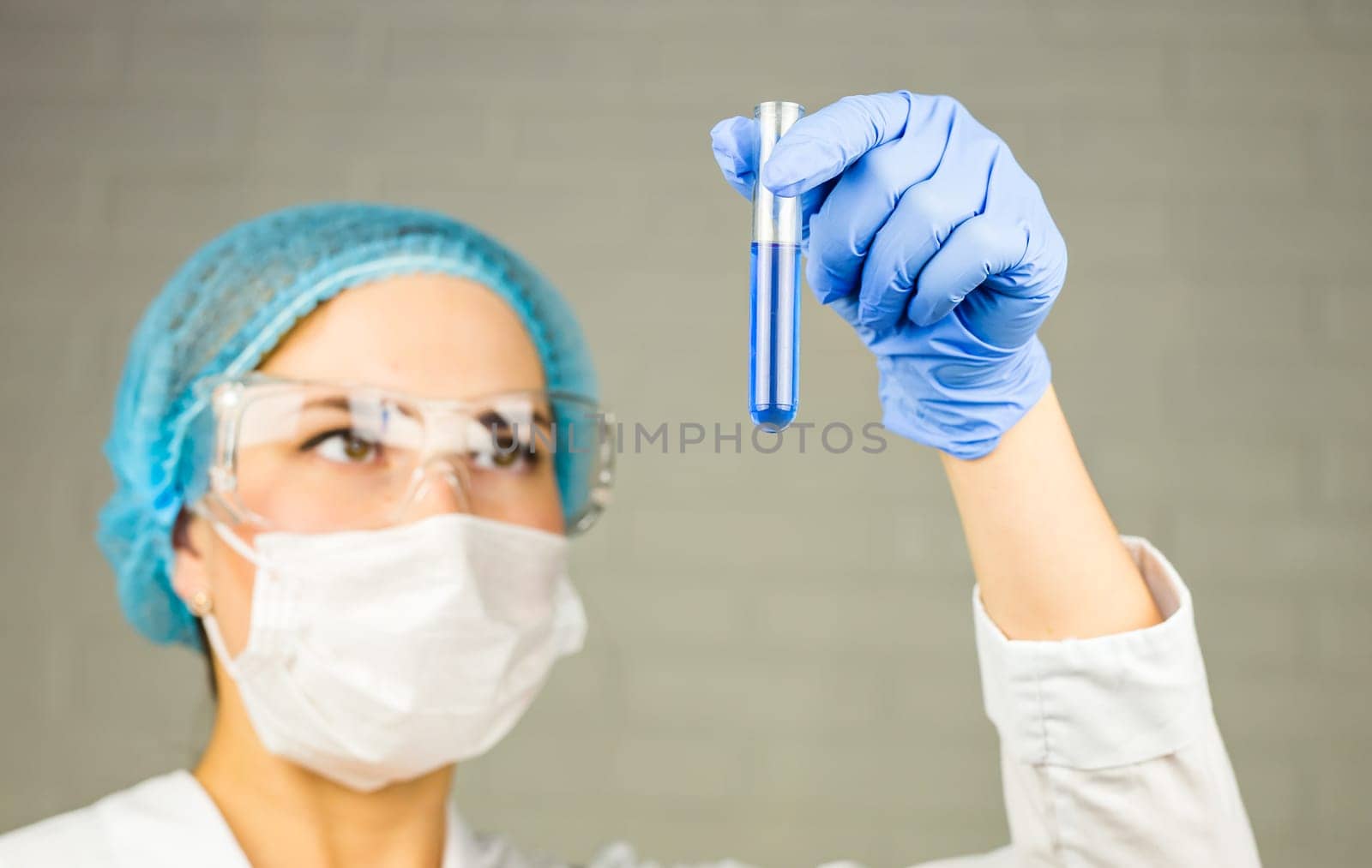 Close-up of glass tube with blue fluid in nurse hand during medical test.