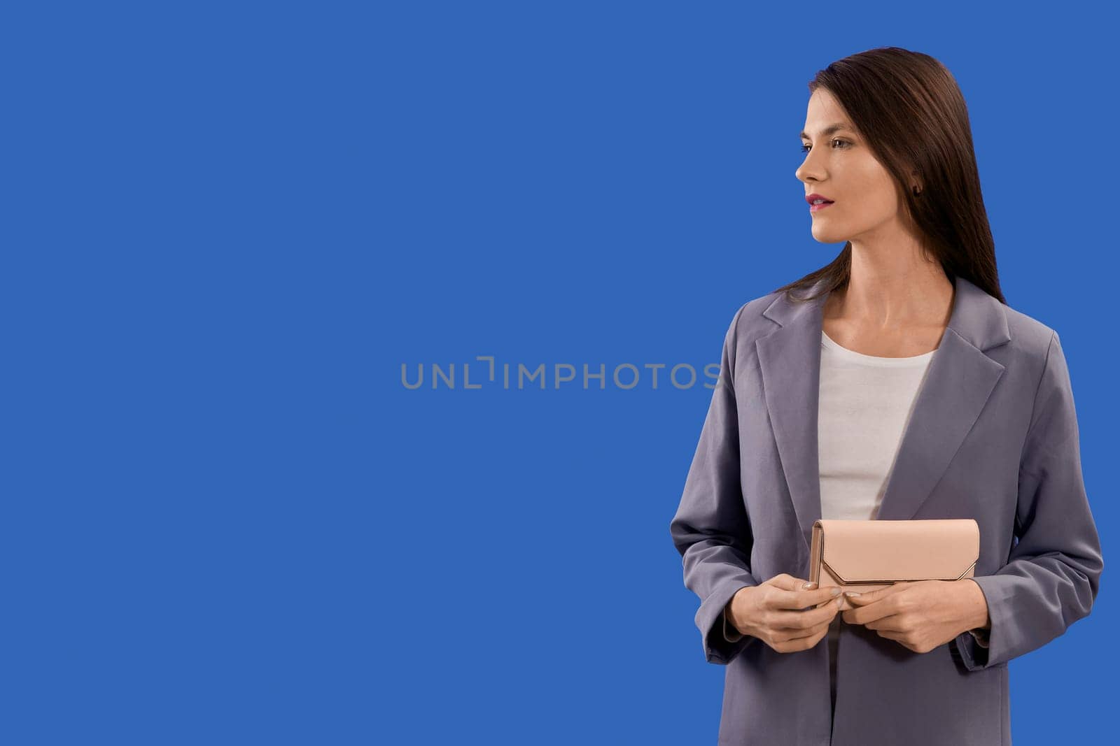 A beautiful young woman is holding a pink purse on a blue background, copy space. High quality photo