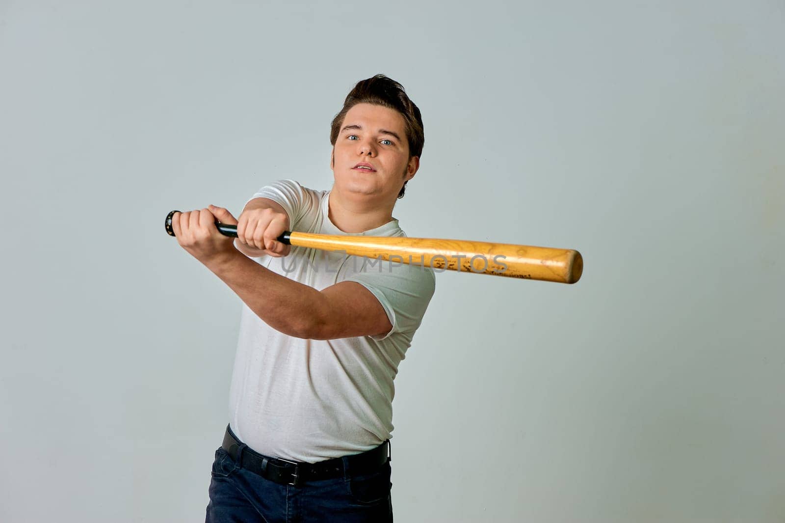 A man with a bat in his hands swings on a gray background. High quality photo