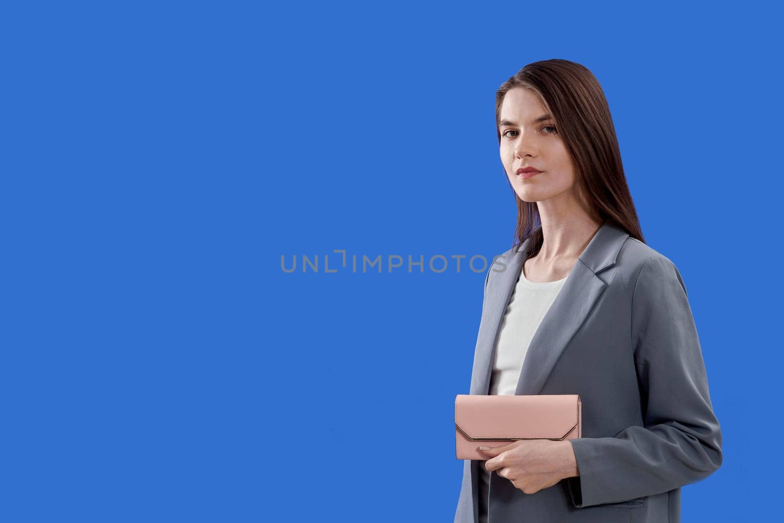 A beautiful young woman is holding a pink purse on a blue background, copy space. High quality photo