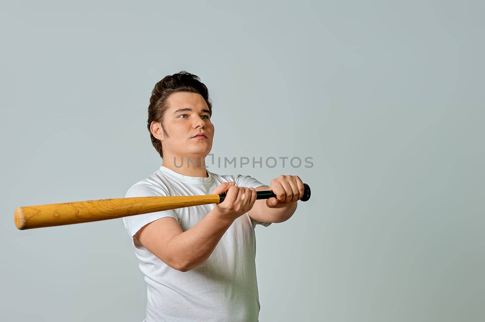 A man with a bat in his hands swings on a gray background. High quality photo