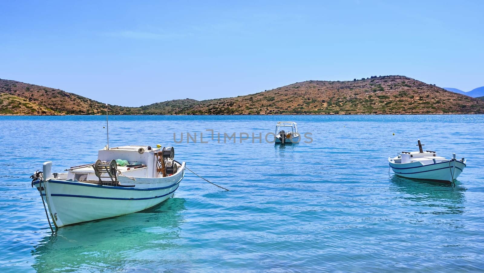 Romantic peaceful view of anchored fishermen's boats on a lagoon and against a hill on a sunny summer day. Crete island, Greece.