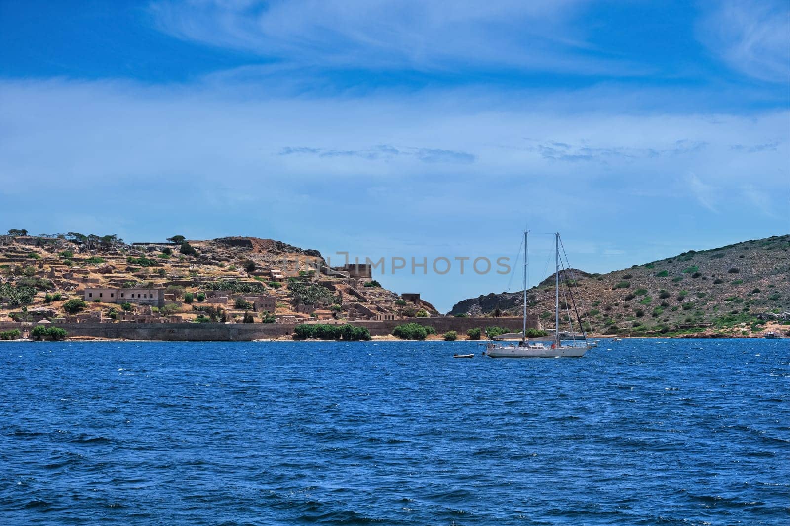 Typical seascape of Spinalonga island, Venetian fortress and floating anchored yacht in front of it on clear sunny summer day, Crete, Greece. film grain