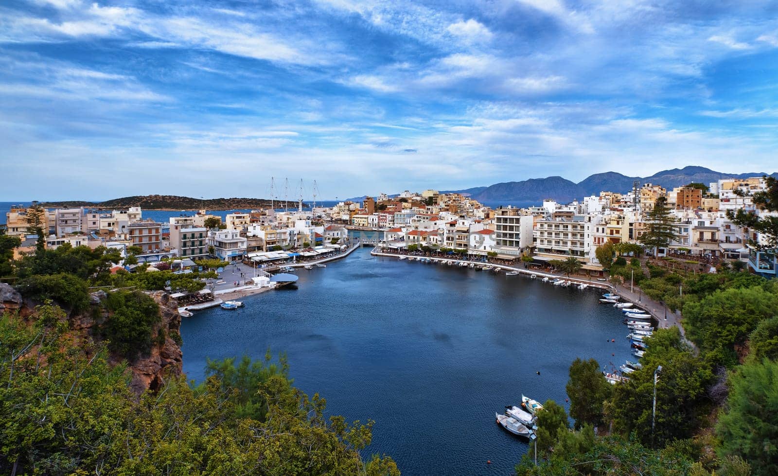 Colorful view of Voulismeni lake and Agios Nikolaos town on Crete island, Greece in evening. Boats, cafes, restaurants, ship, marina, promenade.