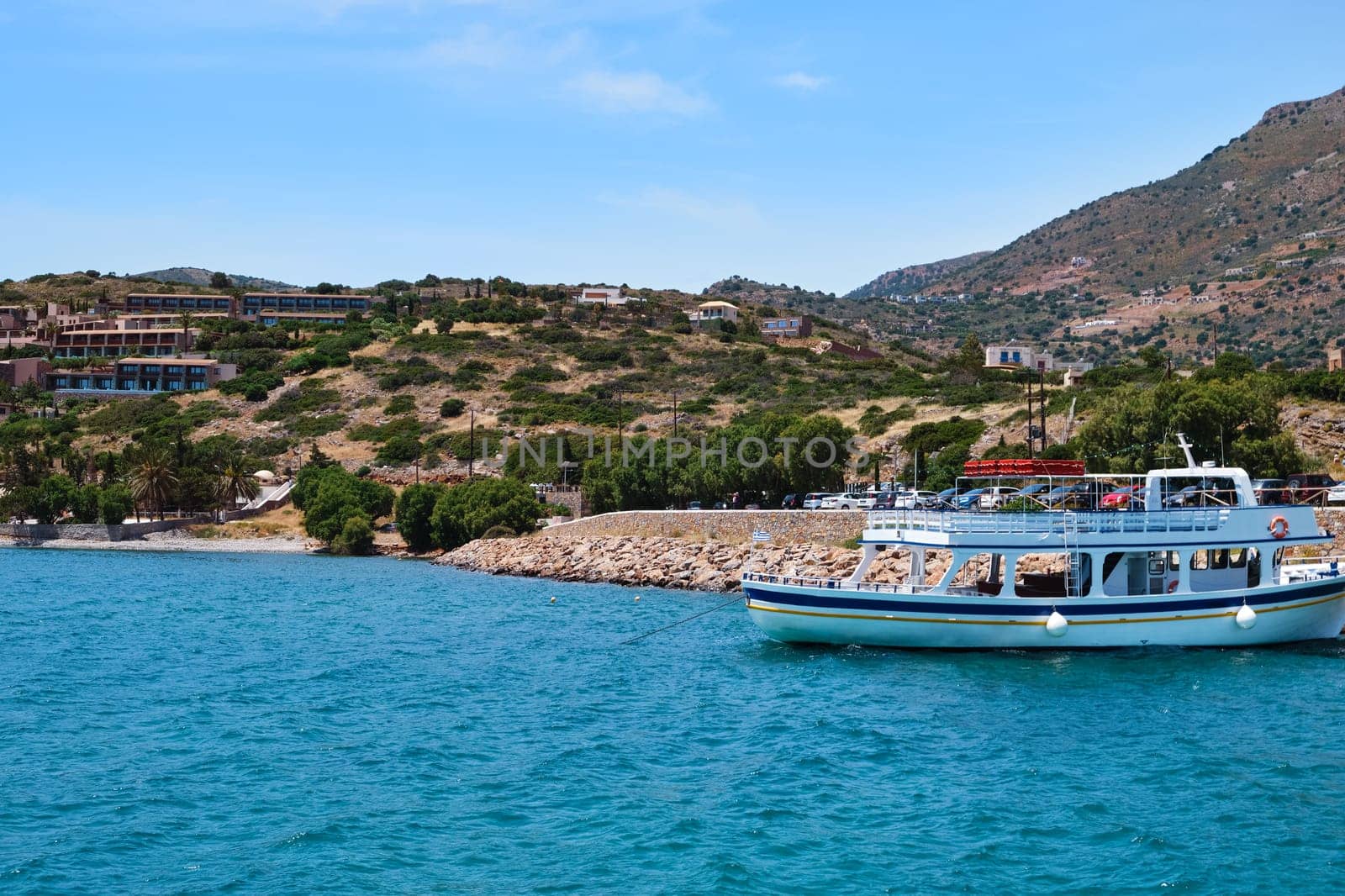 Classic view of beautiful harbor on Greek island of Crete, Greece with hills and houses in background, anchored ferry and calm blue sea on clear sunny summer day