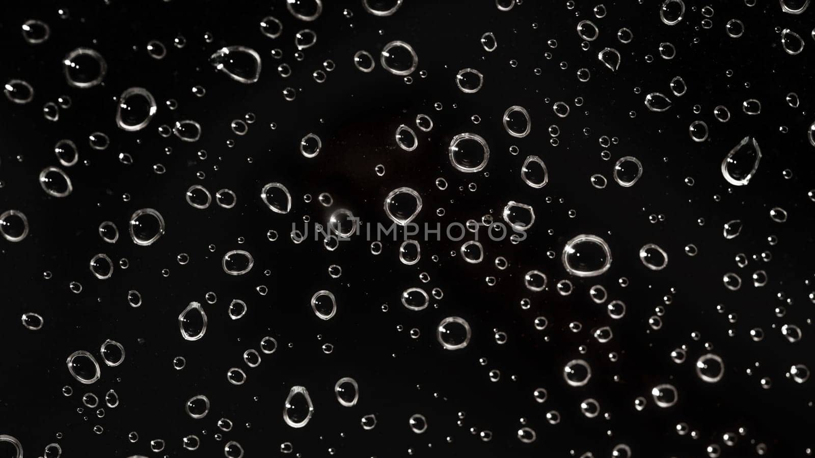 Closeup - rain water drops behind glass look like bubbles in black liquid. Abstract wet background.