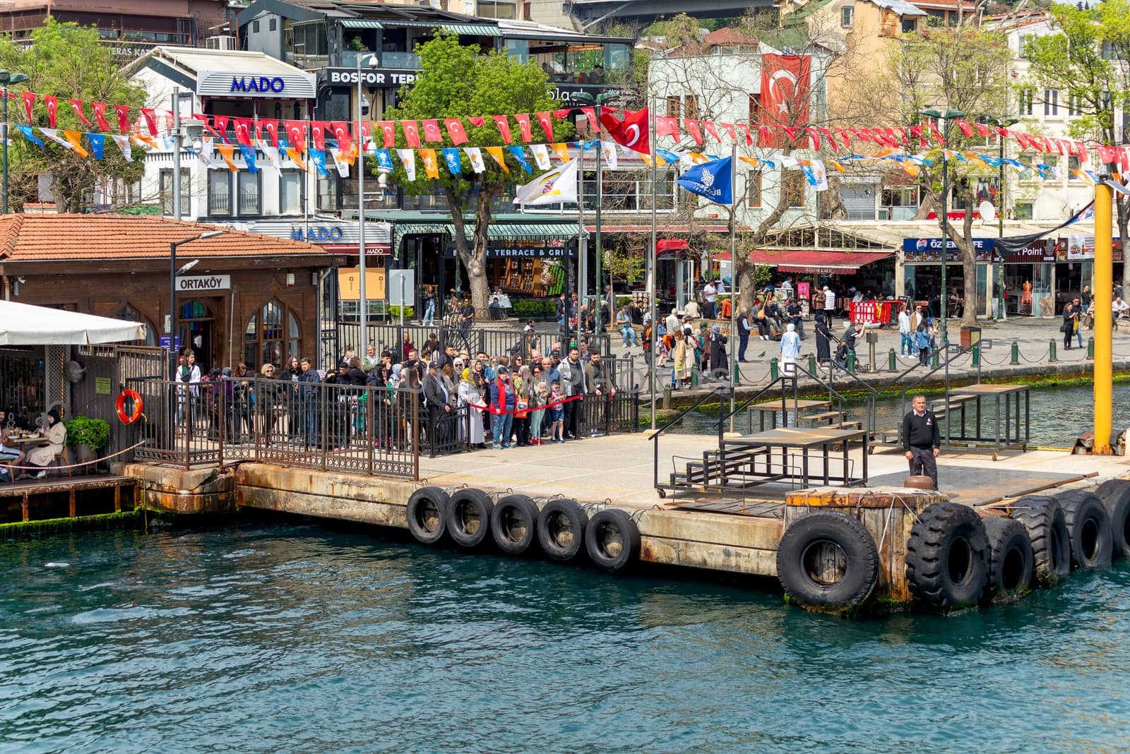Istanbul, Turkey - May 8, 2023: Bosphorus Strait, Ortakoy Ferry Terminal with passengers waiting for ferry, and crowded Ortakoy square in the background