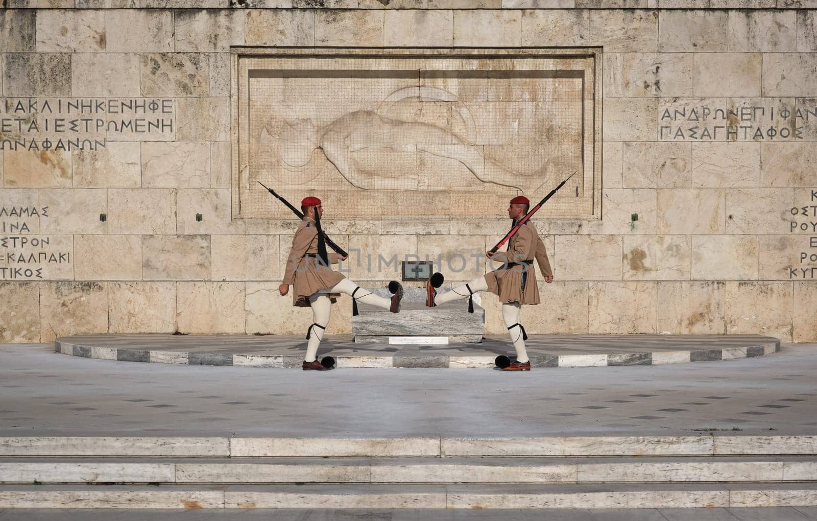 Ceremony of Presidential guard Evzones by the Greek tomb of Unknown Soldier. Evzones in summer uniform face each other, legs up. Close shot.