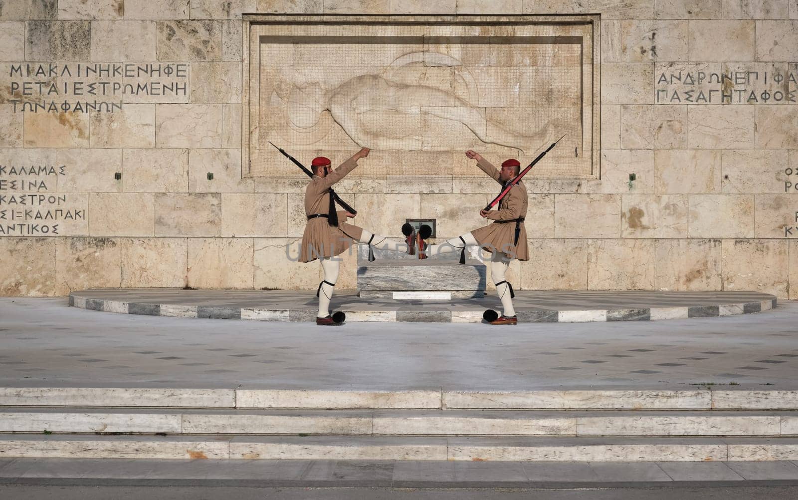 Ceremony of Presidential guard Evzones by the Greek tomb of Unknown Soldier. Evzones in summer uniform face each other, legs up, hands up. Close shot.