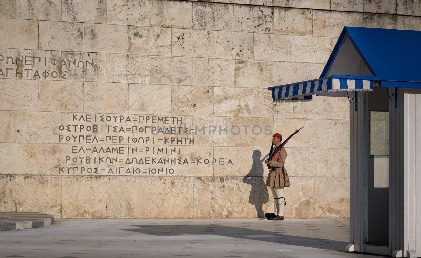Evzone stand still on guard, by the wall of the tomb of Unknown soldier next to guard box in afternoon.