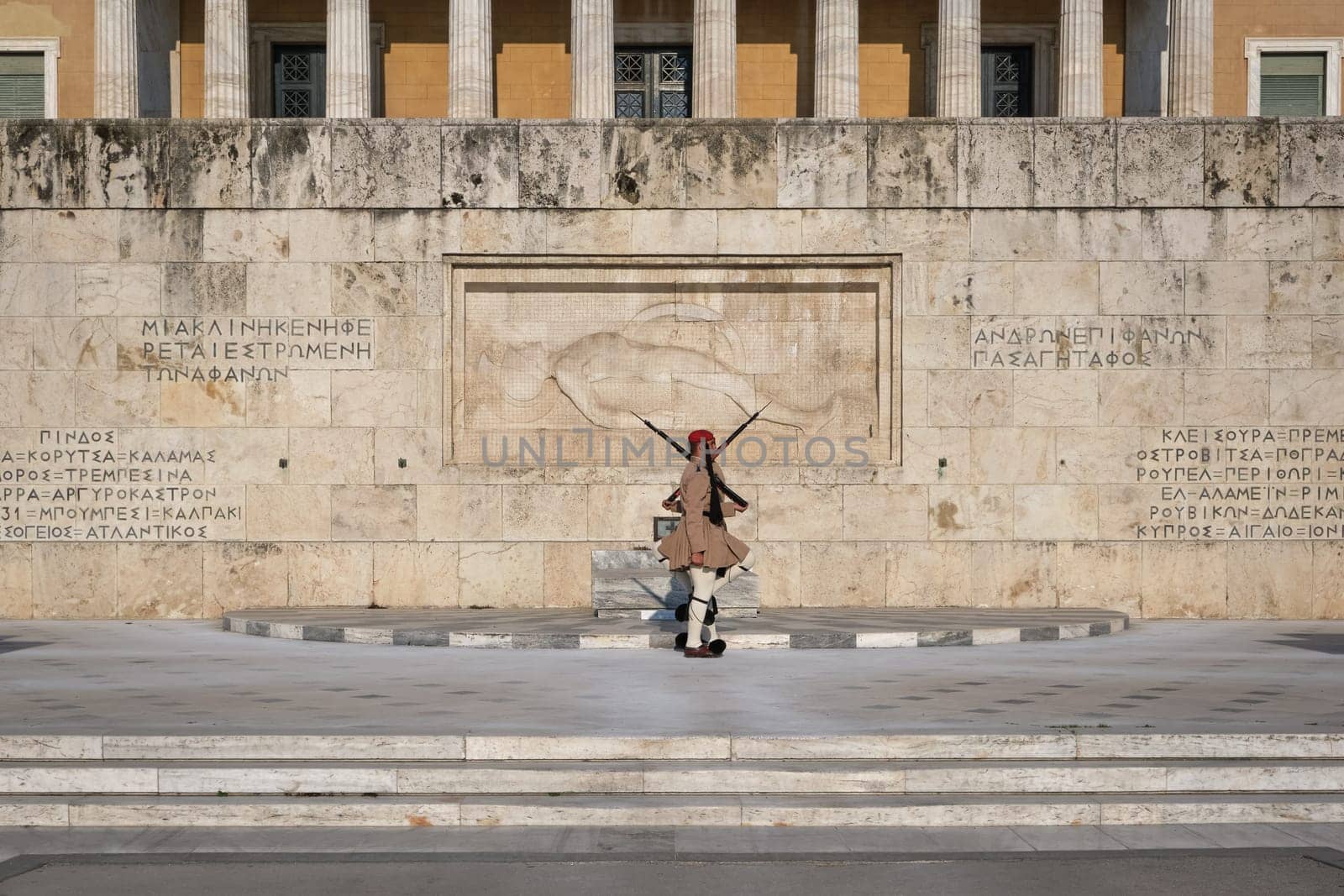 Ceremony of Presidential guard Evzones by the Greek tomb of Unknown Soldier. Evzones in summer uniform stand as one, knees up. Wide shot.