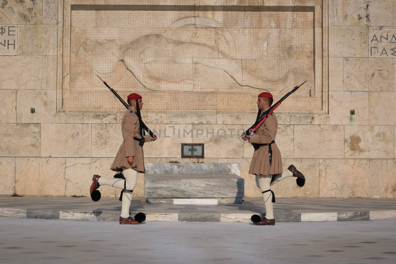 Ceremony of Presidential guard Evzones by the Greek tomb of Unknown Soldier. Evzones in summer uniform face each other, knees bent . Close-up shot.