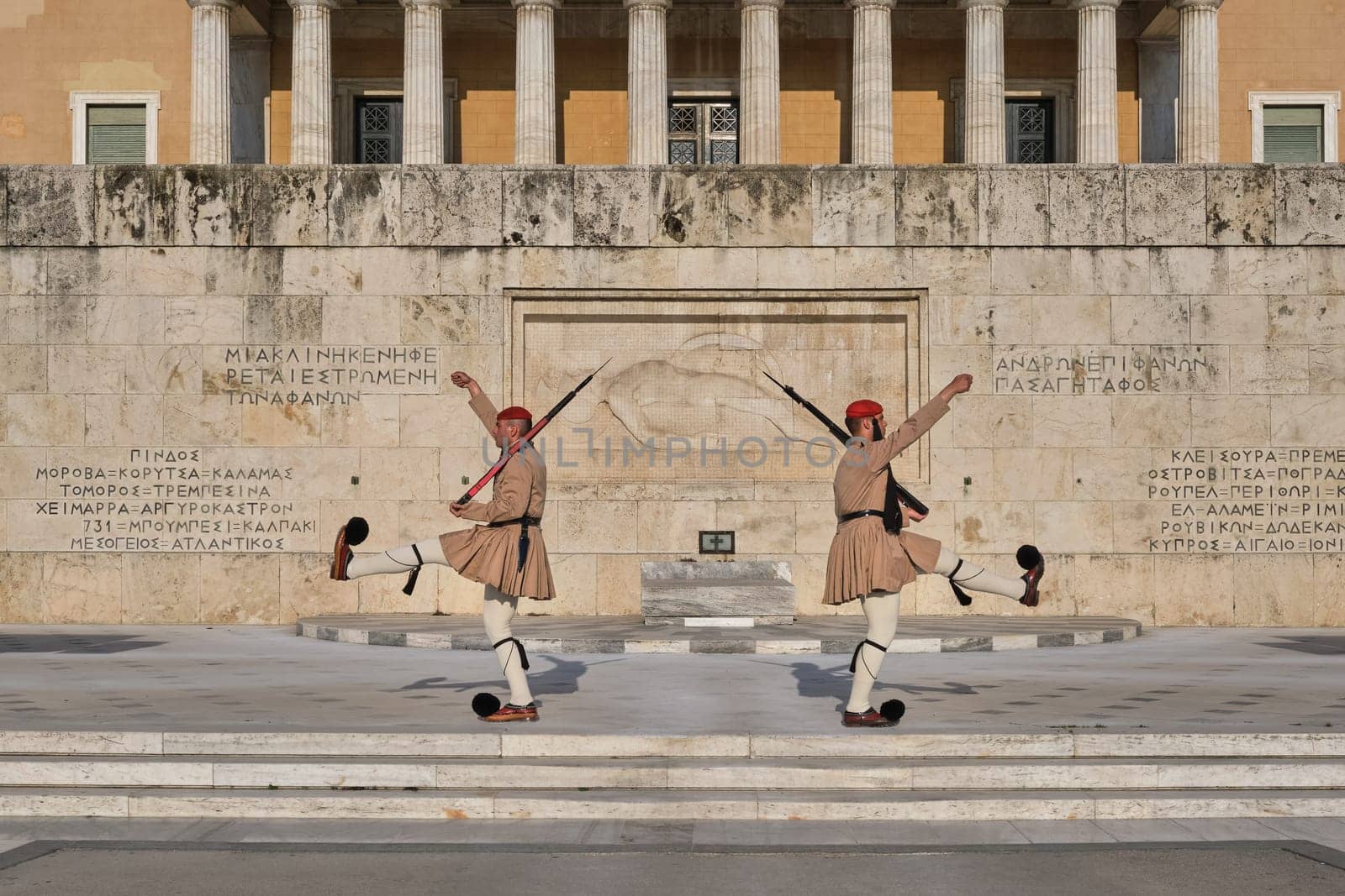 Ceremony of Presidential guard Evzones by the Greek tomb of Unknown Soldier. Evzones in summer uniform separate, hands up, legs up. Wide shot.