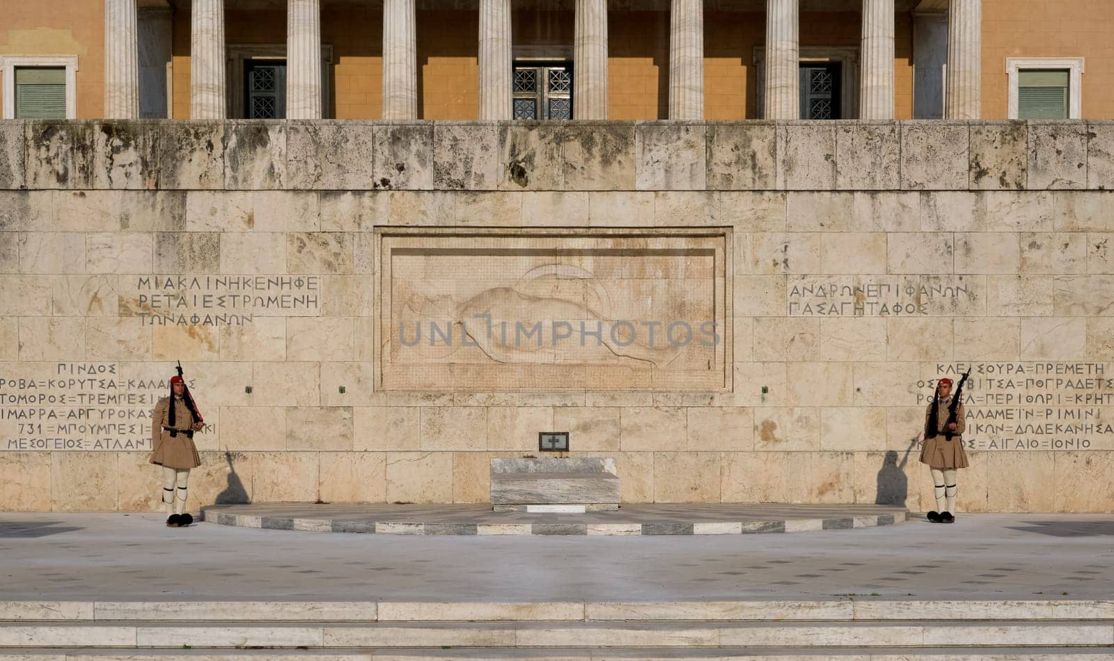 Evzones in summer uniform stand still on guard either side of the Tomb of Unknown soldier in afternoon. Wide shot.