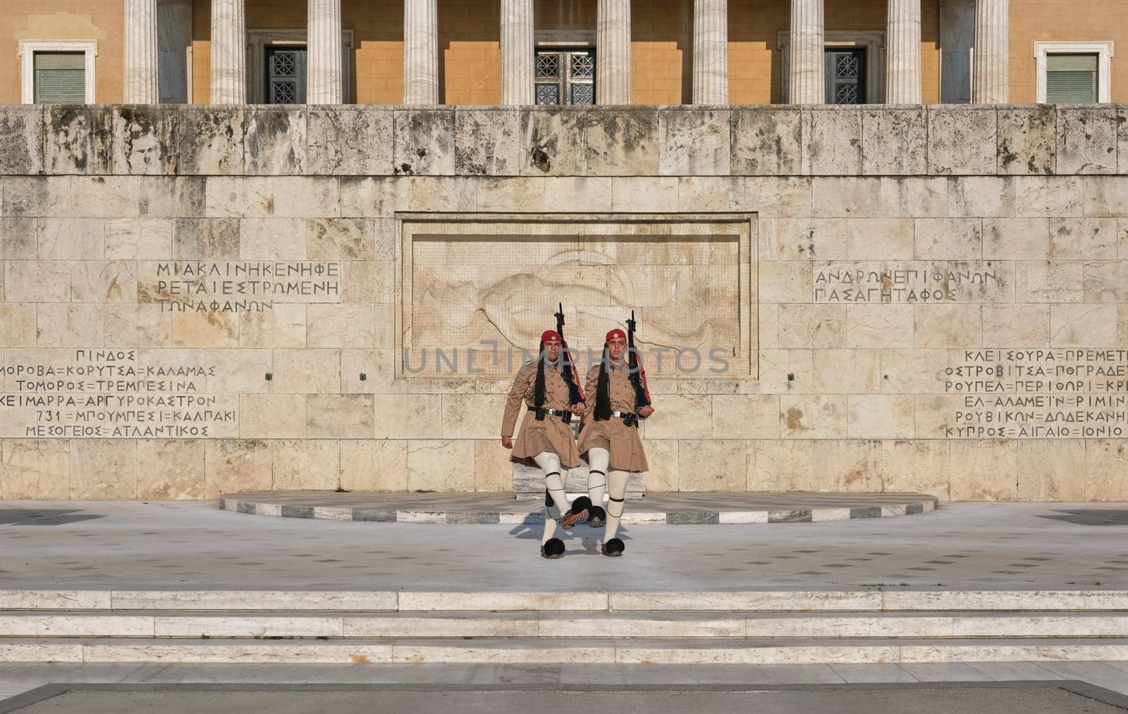 Evzone stand in front of Tomb of Unknown Soldier, legs up, shoes touching. Wide shot
