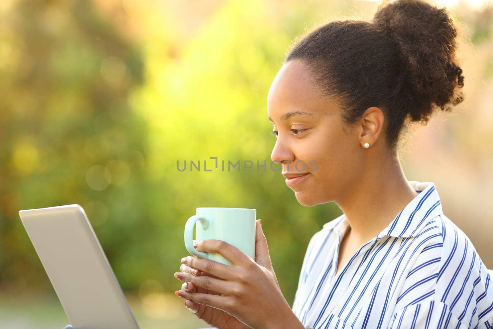 Black woman drinking coffee and using laptop in a park