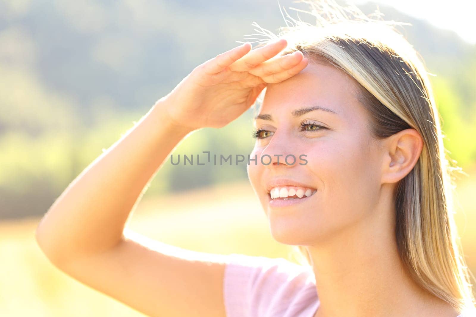 Happy woman with hand on forehead protects from sun in nature