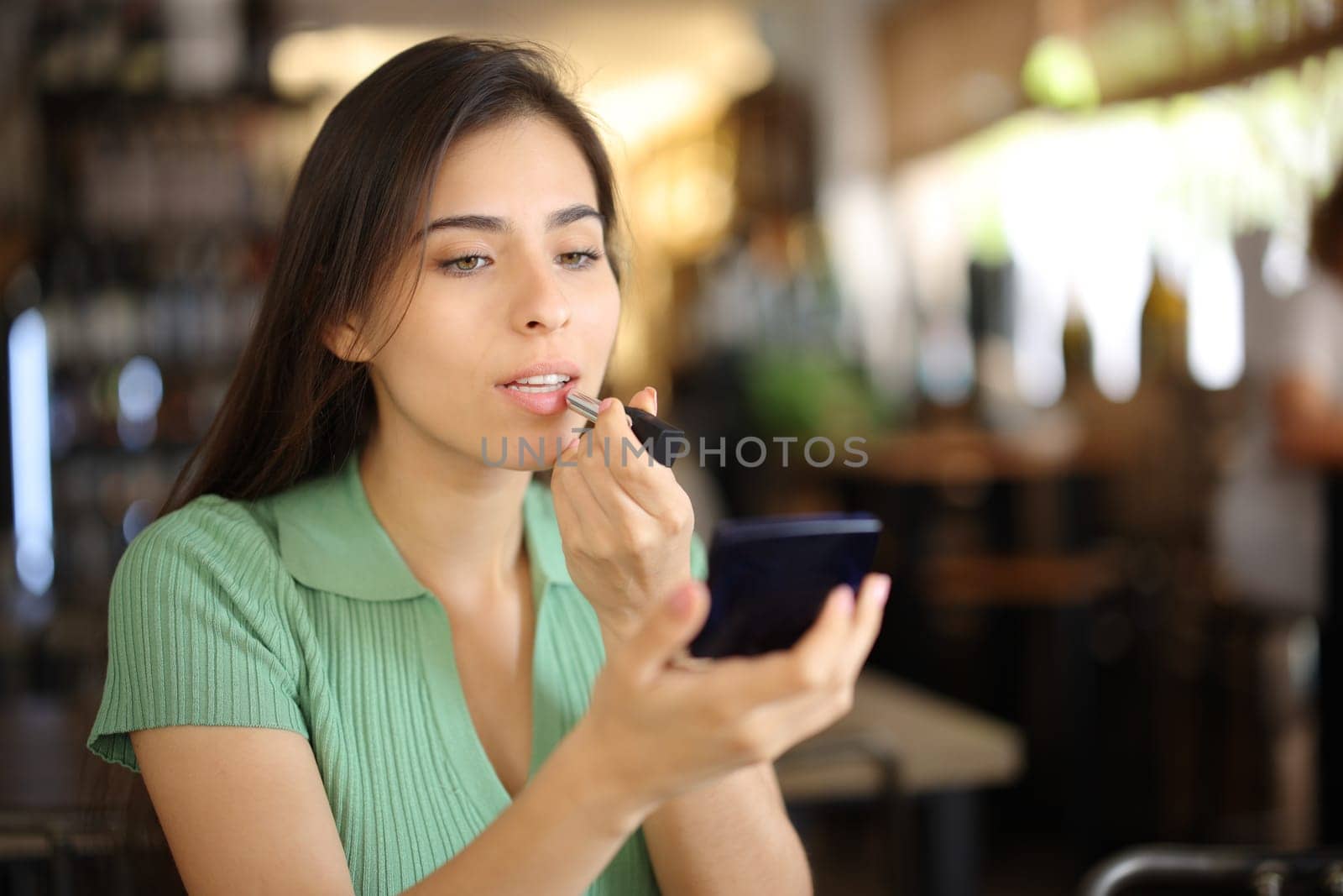 Woman painting lips before dating in a restaurant interior