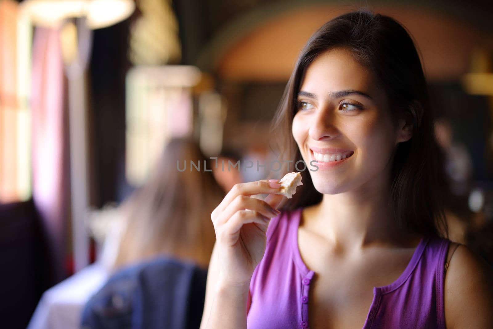 Happy woman eating some bread in a restaurant looking at side