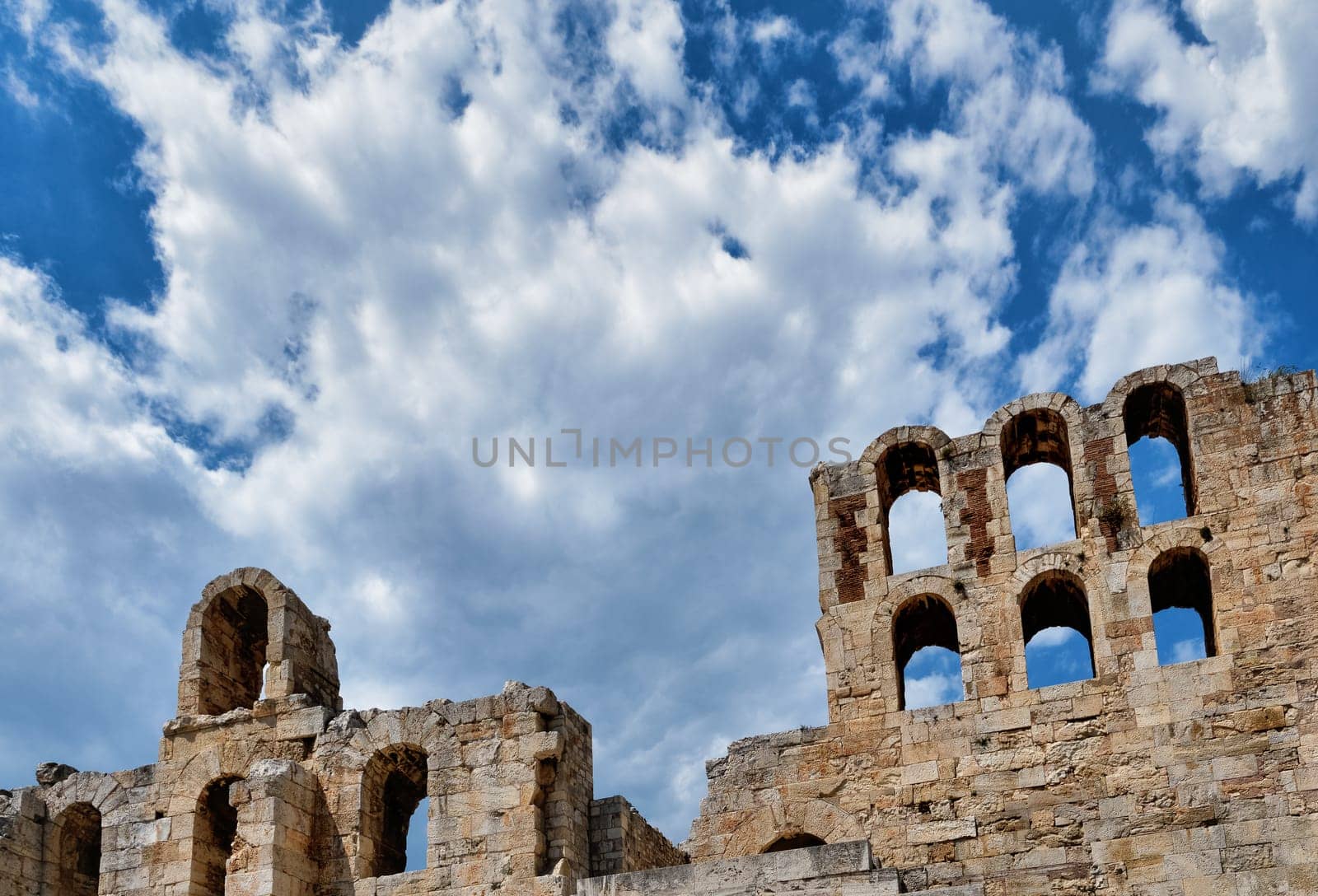 Diagonal dynamic composition of Odeon of Herodes Atticus theater arches on Acropolis hill, Athens, Greece, against bright blue sky and super clouds. Ancient ruins still used as venue for concerts, performances and festivals. UNESCO world heritage.
