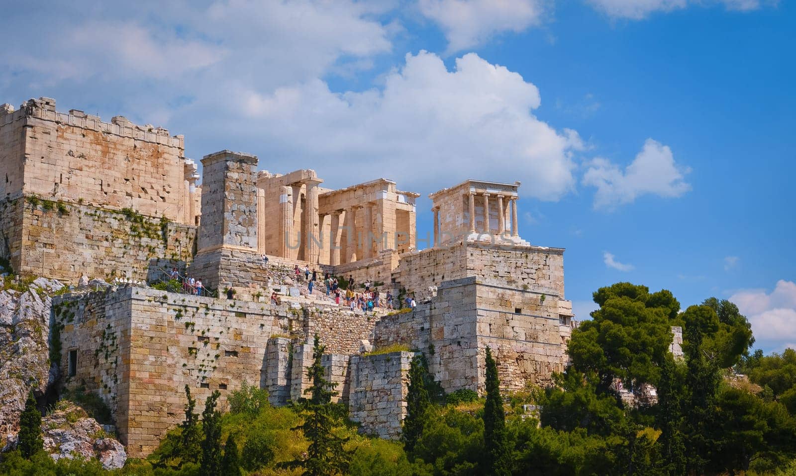 View of Acropolis hill from Areopagus hill in summer daylight with great clouds in blue sky, Athens, Greece. UNESCO world heritage. Propylaea entrance, Agrippa's monument, Parthenon. Fresh green foliage. Close shot