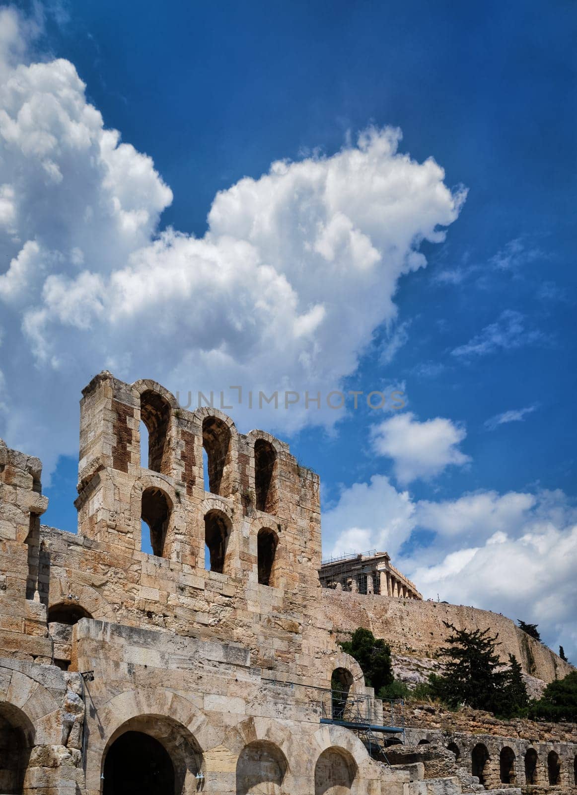 Diagonal dynamic composition of Odeon of Herodes Atticus theater arches on Acropolis hill, Athens, Greece, against bright blue sky and super clouds. Ancient ruins still used as venue for concerts and festivals. UNESCO world heritage. Vertical shot.
