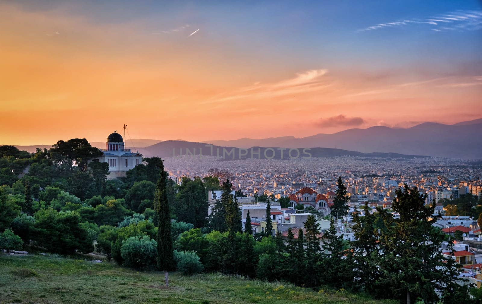 Beautiful and colorful view of Athens, Greece and its residential areas from Pnyx hilltop in soft evening sunlight and great sunset sky. National observatory of Athens in foreground.
