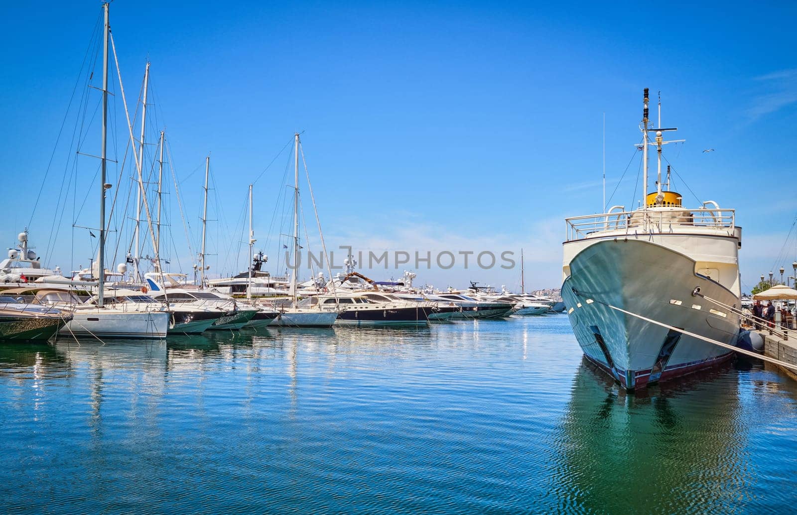 Boats and yachts anchored or moored in Athens marina and by its promenade in Glyfada on a bright summer day. Concept of seascape, voyage, sea adventure, private yachting weekend, summer vacations. Athens, Greece