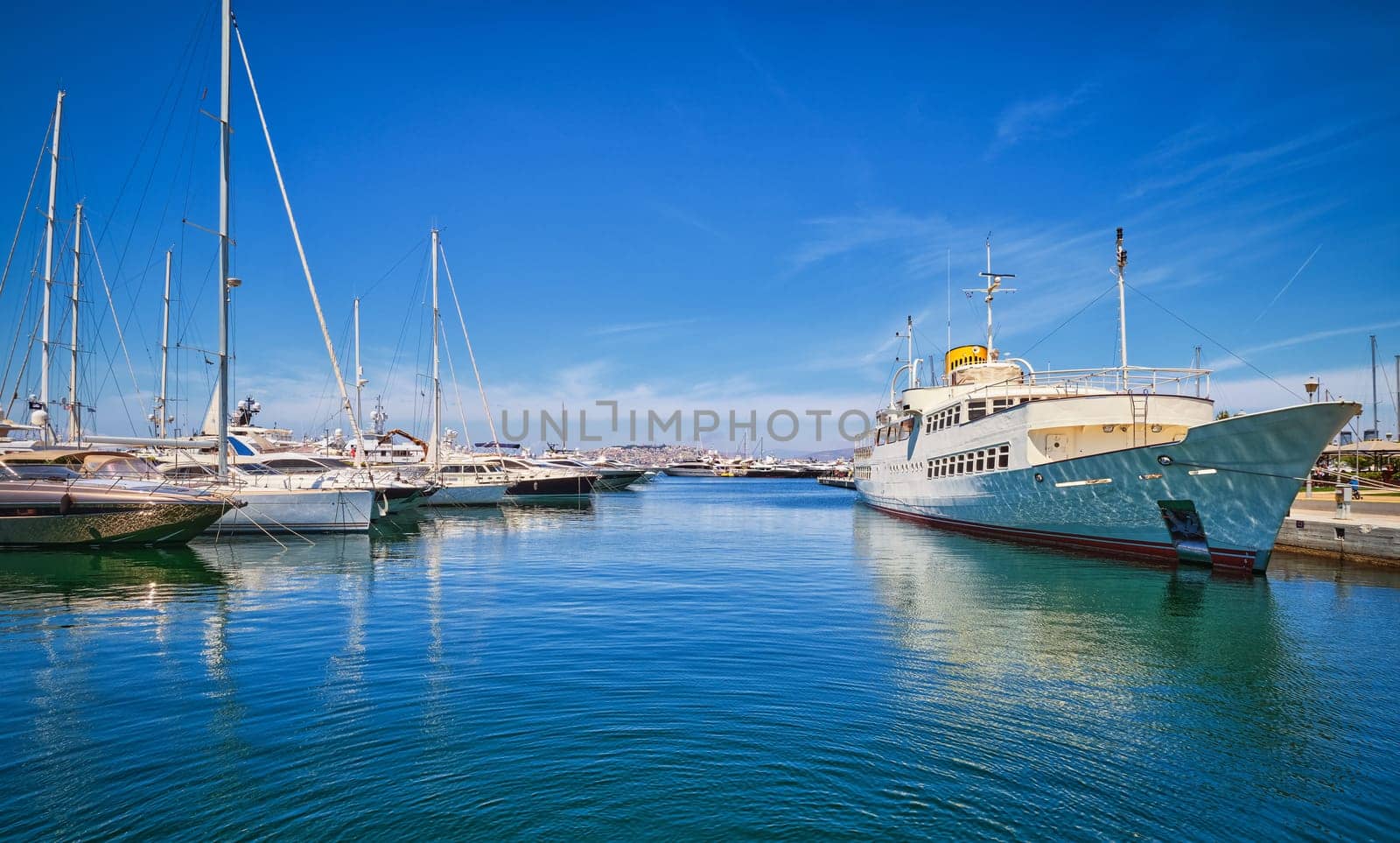 Boats and yachts anchored or moored in Athens marina and by its promenade in Glyfada on a bright summer day. Concept of seascape, voyage, sea adventure, private yachting weekend, summer vacations. Athens, Greece