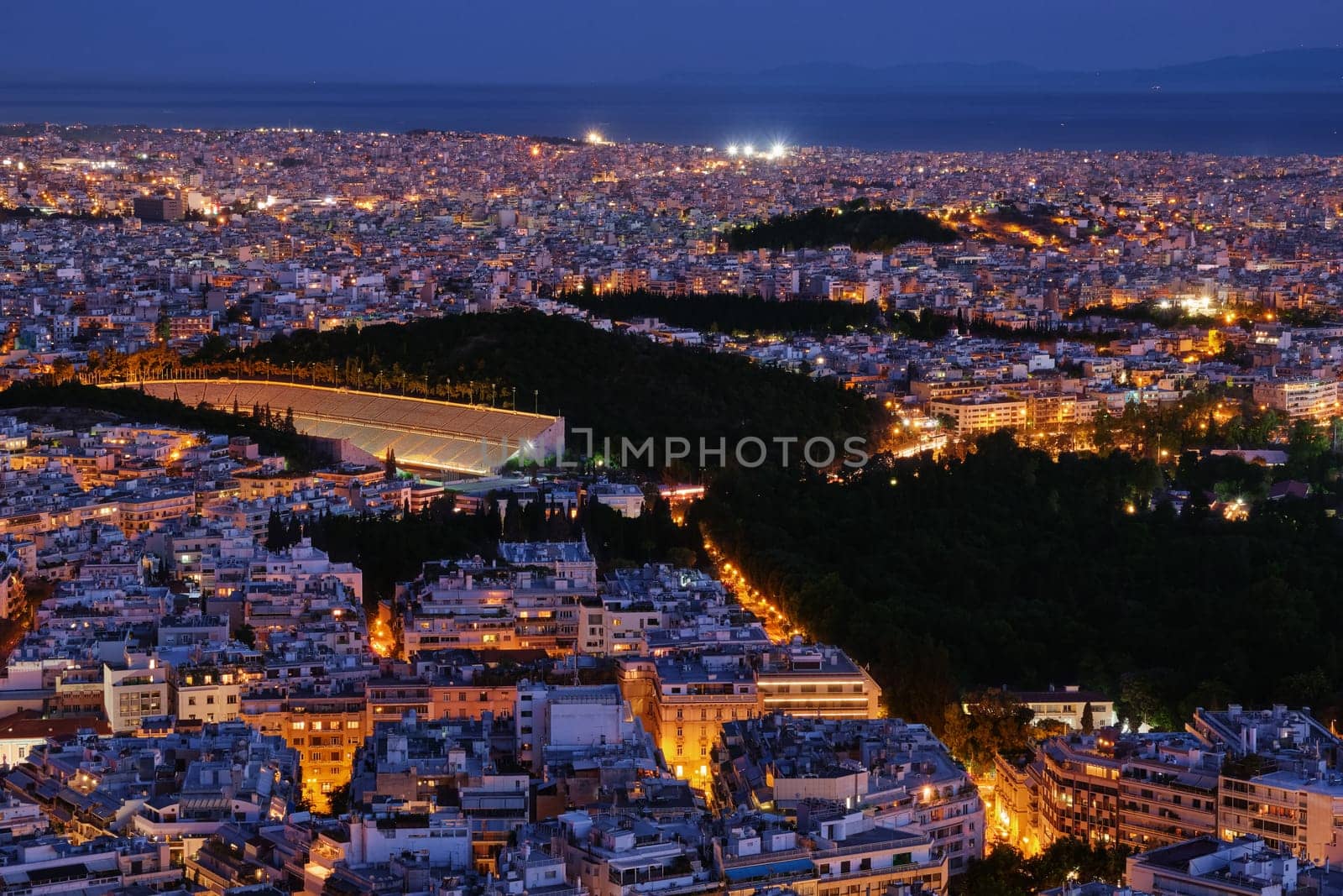 Night view of Athens, Greece with ancient and restored Panathenaic stadium of Kallimarmaro, shot form hill of Lycabettus. Beautiful city at blue hour, iconic site for Olympic games movement. National Garden in center of city.