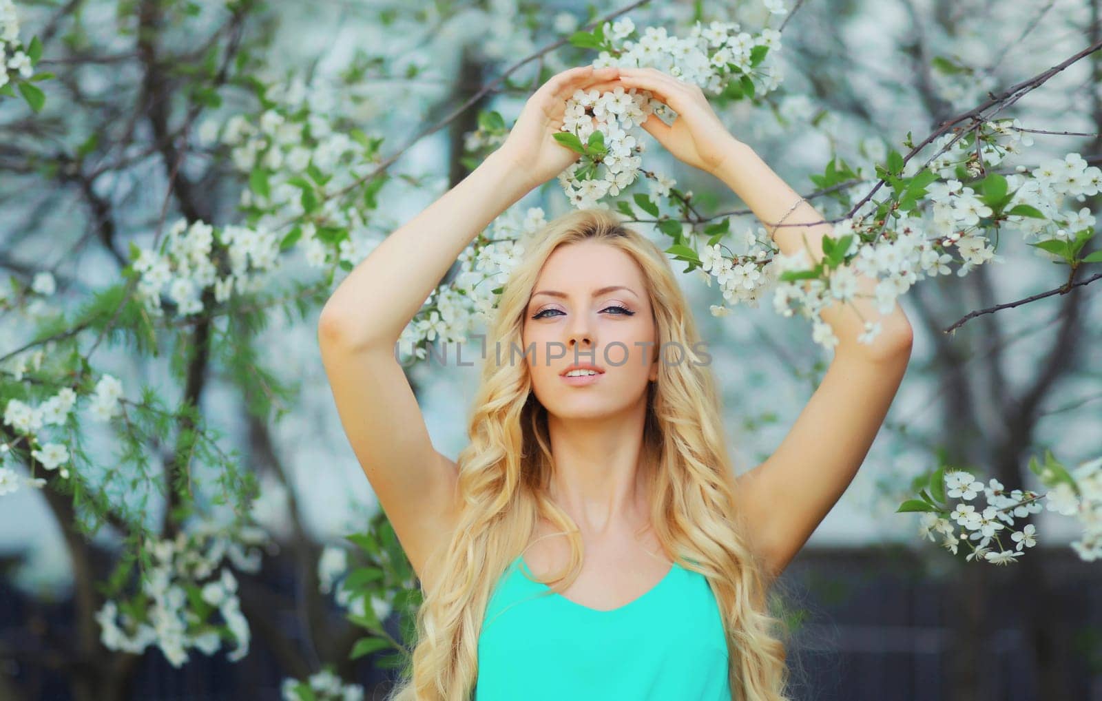 Beautiful young woman with blonde long hair in spring blooming garden on a sunny day against flowers trees background