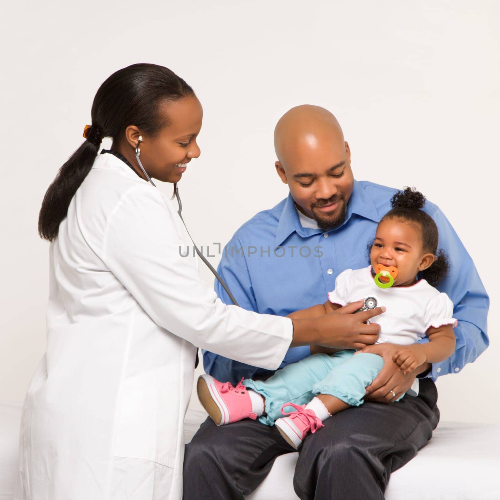 African-American female pediatrician examining baby girl being held by father.