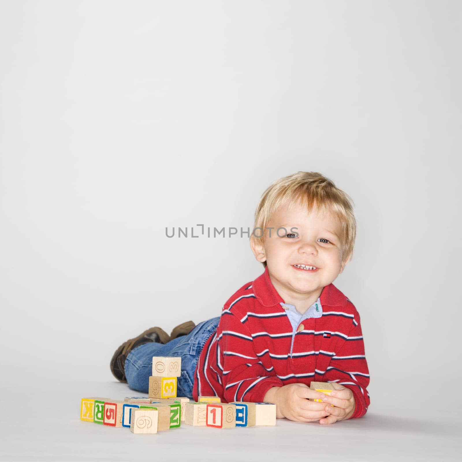 Studio portrait of Caucasian boy lying on stomach propped up on elbows playing with toy blocks.