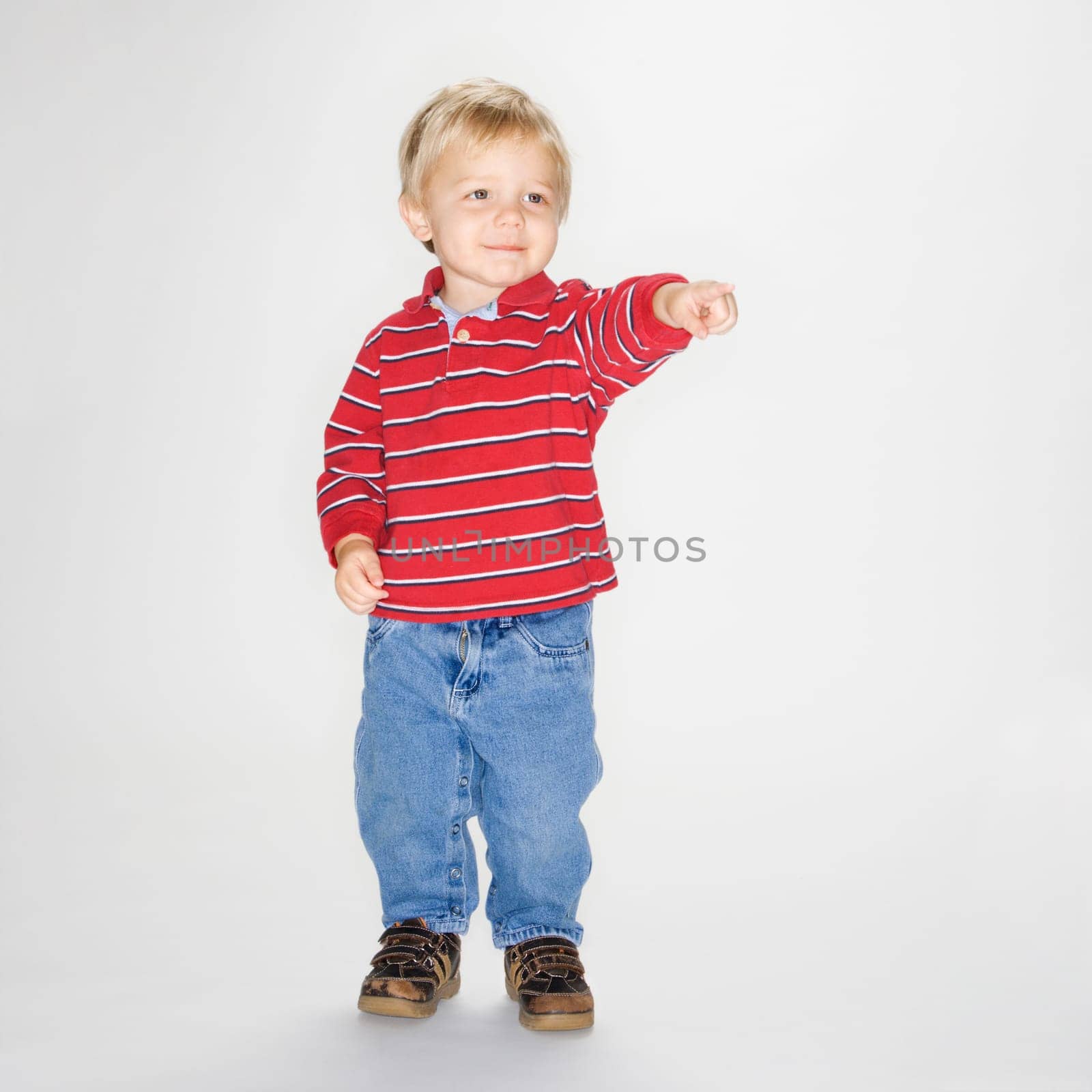 Studio portrait of Caucasian boy standing and pointing against white background.