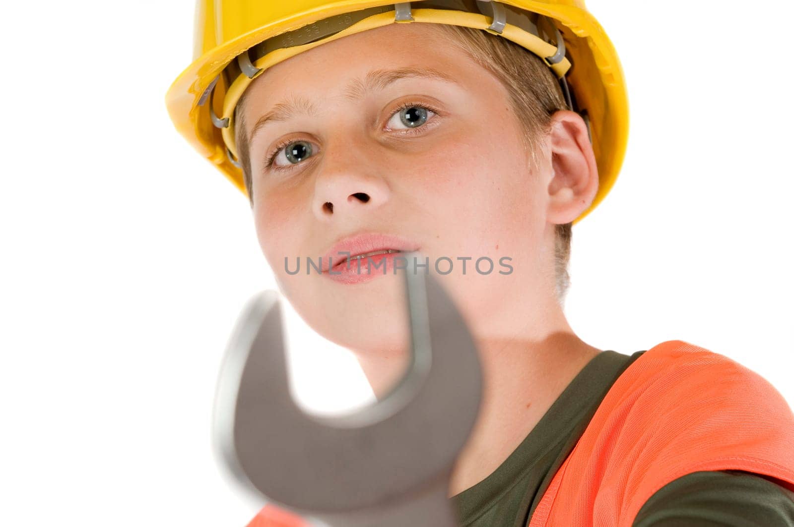 Head and shoulders view of a young teenage boy wearing a yellow hardhat showing a spanner at the camera with shallow depth of field isolated on white.