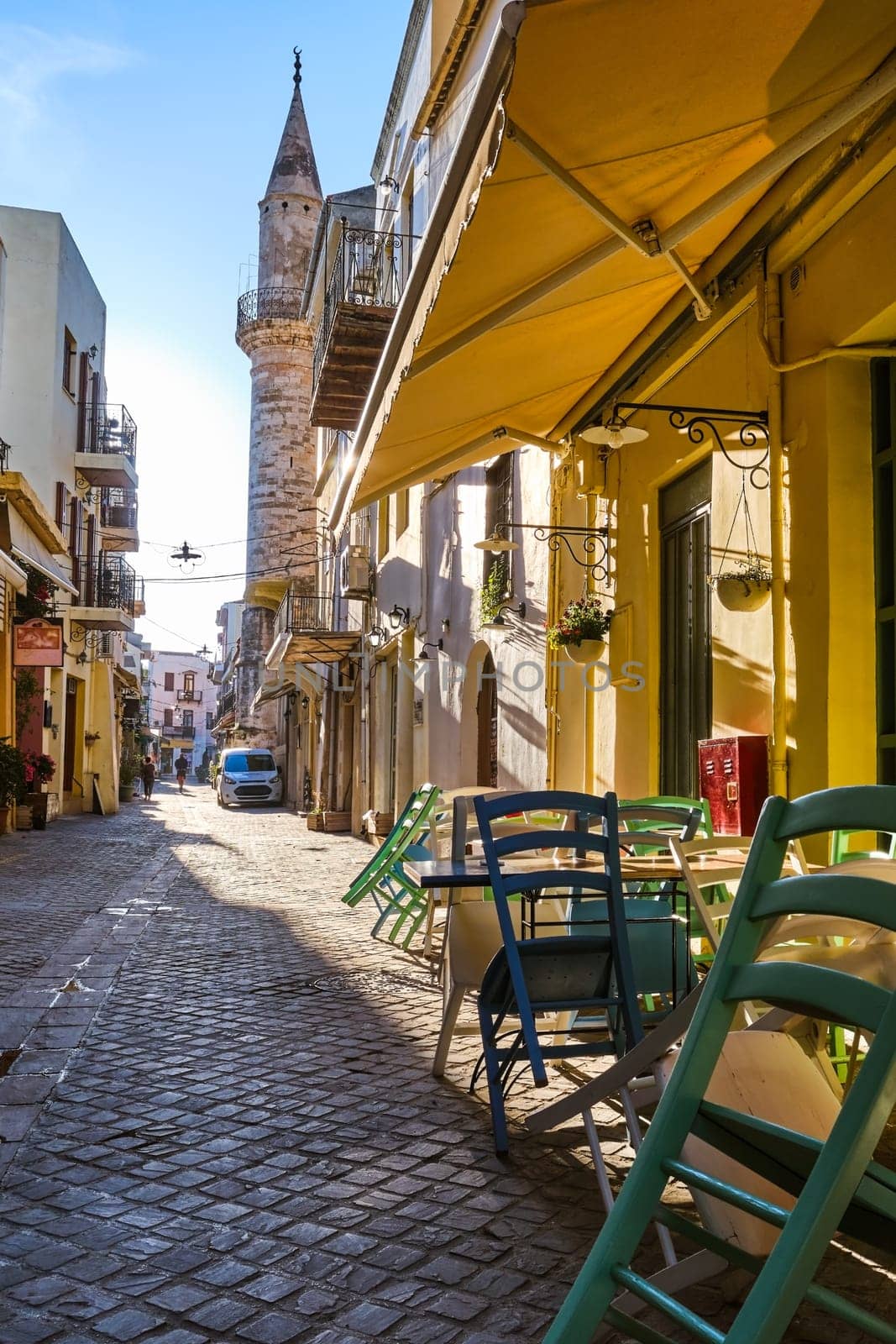 Early morning in old narrow streets of Chania, Crete, Greece and historical monument of Ottoman era - Ahmet aga minaret in middle of street. Cafes and restaurant ready to open.