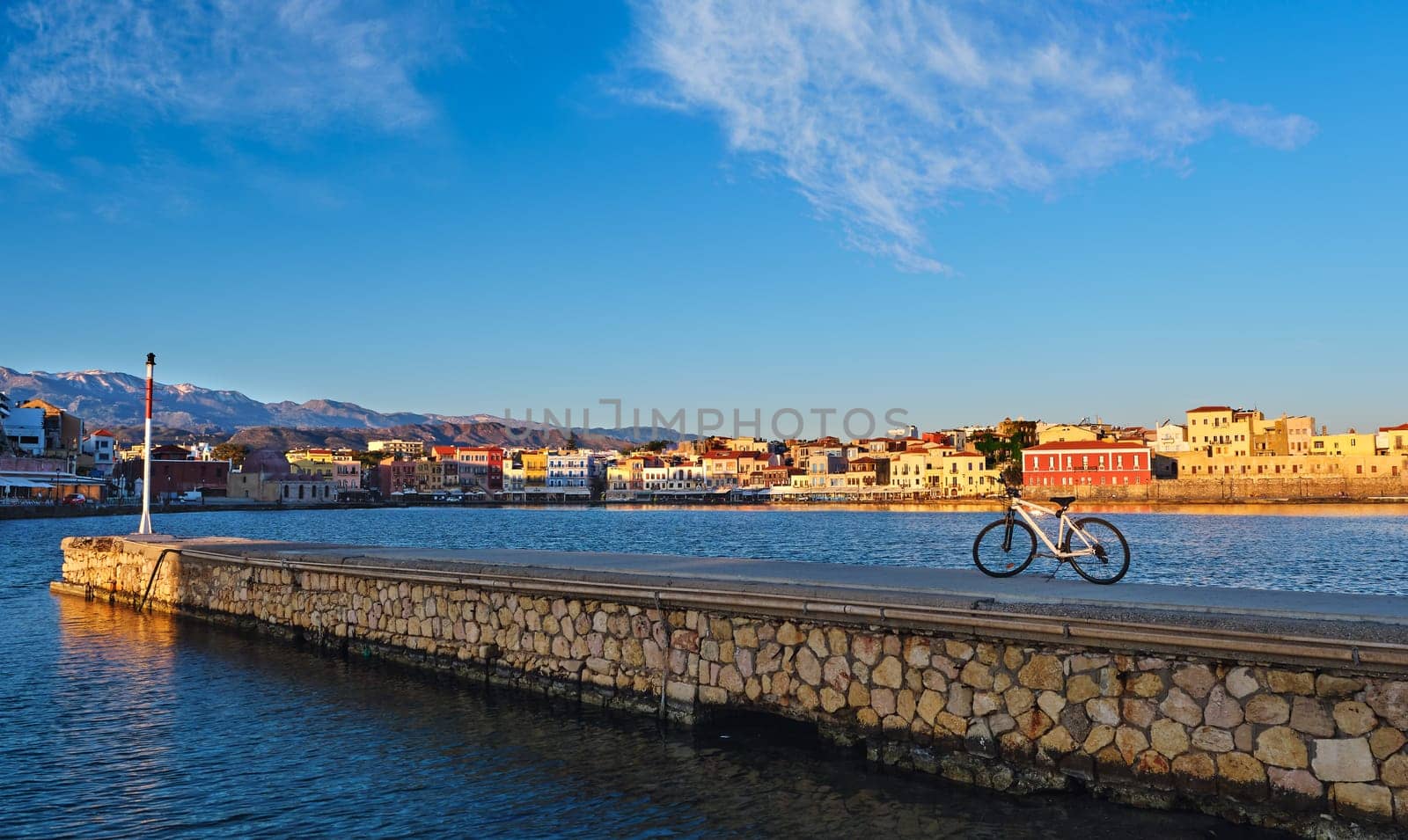 Early morning in Old Venetian harbour of Chania, Crete, Greece. Pier and bicycle in foreground. Chania waterfront promenade and Cretan mountains in background. Golden hour. Bicycle tours, cycling, sightseeing rides. Healthy lifestyle, morning rides
