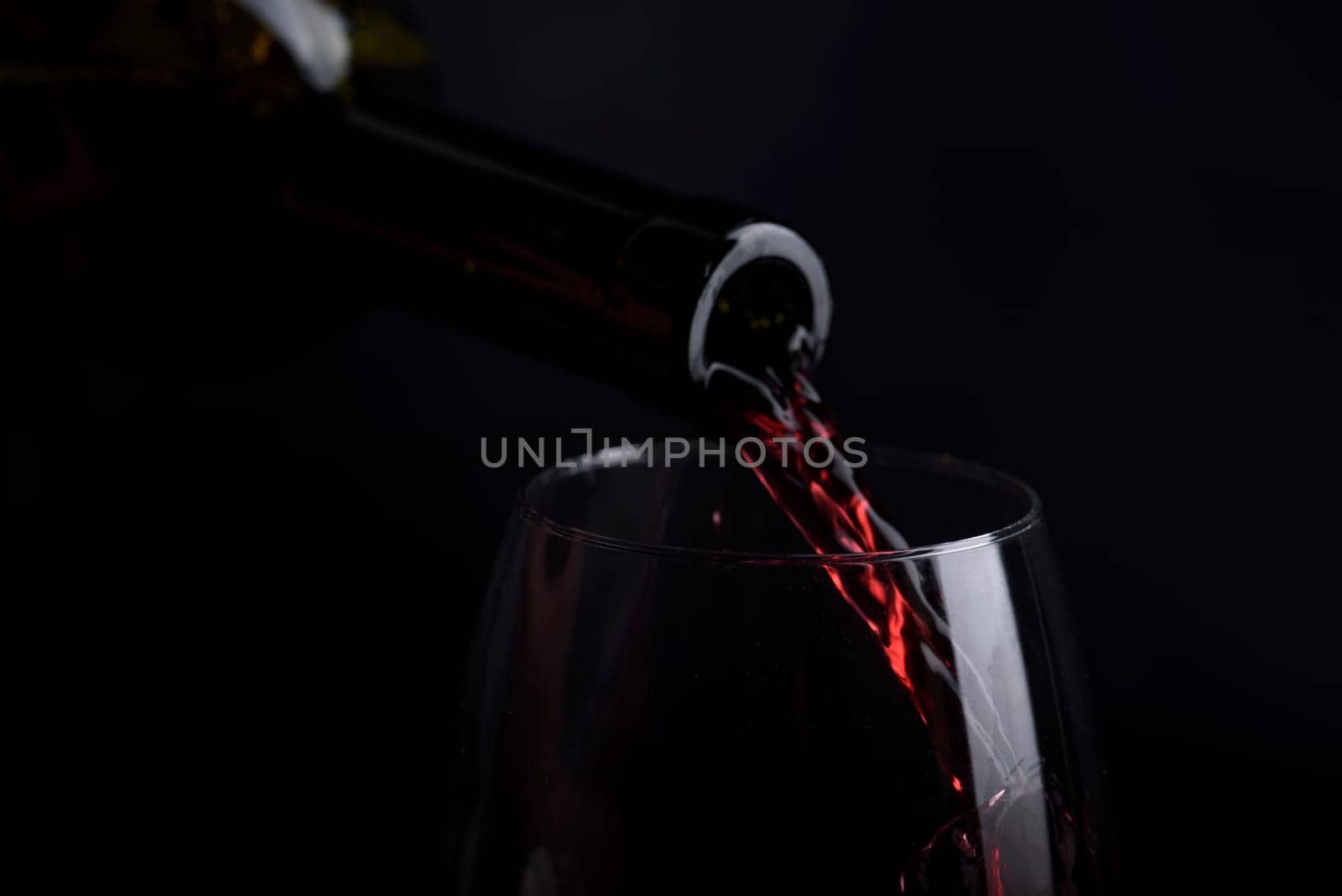 Red wine pouring in wine glass over black background. Closeup of red wine splashing in wineglass in restaurant. Wine tasting.