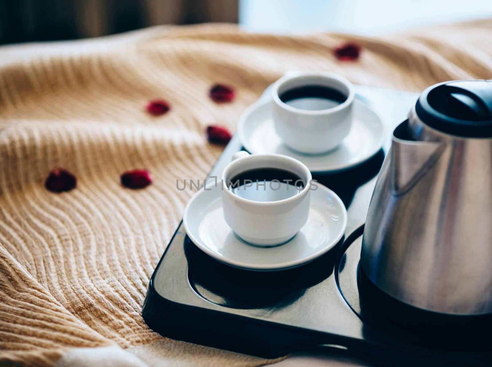 Morning breakfast with black coffee in bedroom. Two cups of coffee on bed decorated with rose petals in luxury hotel bedroom.