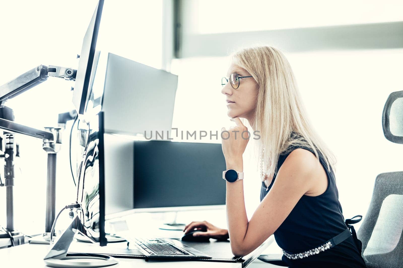 Female stock broker trading online watching charts and data analyses on multiple computer screens