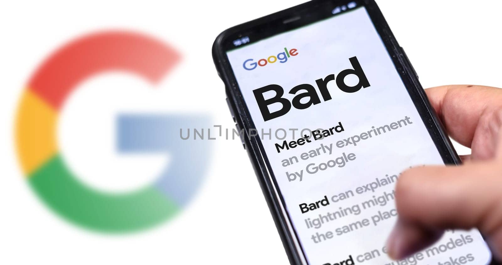 San Francisco US, May 12 2023: A hand holding a phone with the Google Bard website on the screen. White background with blurred Google logo. Bard is Google artificial intelligence chatbot