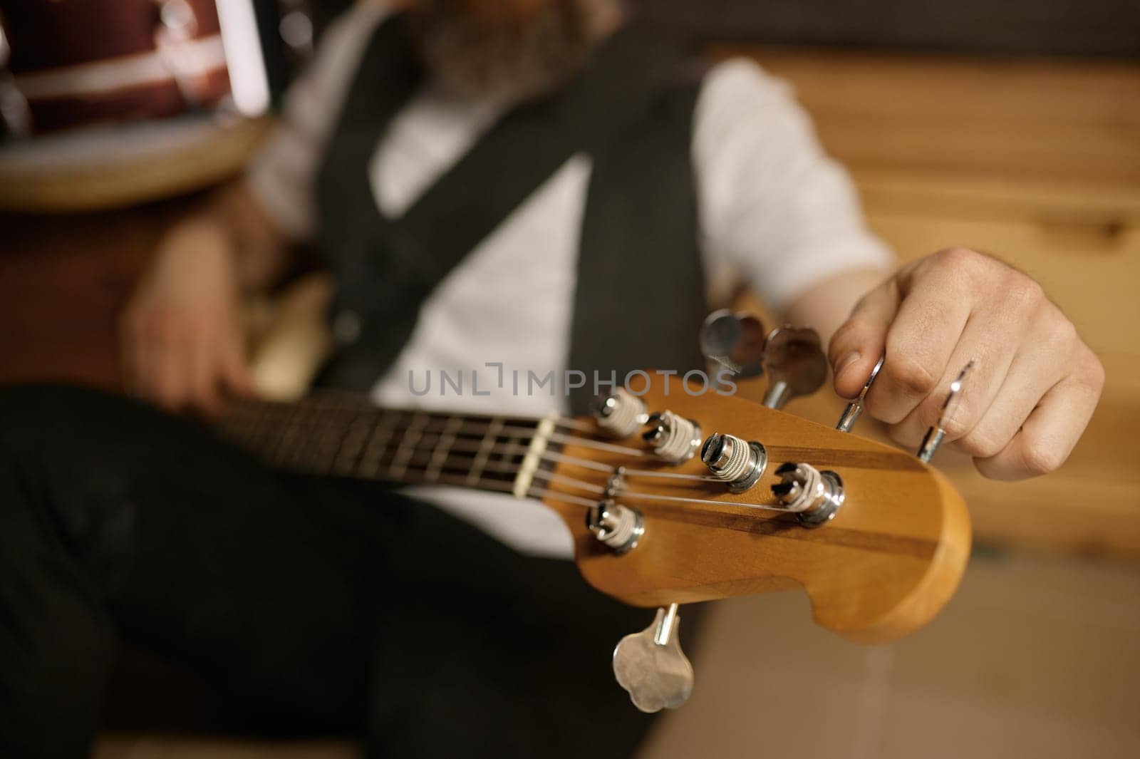 Bearded bald guitarist tuning his musical instrument while sitting on floor. Brutal rockstar rest and preparing for training