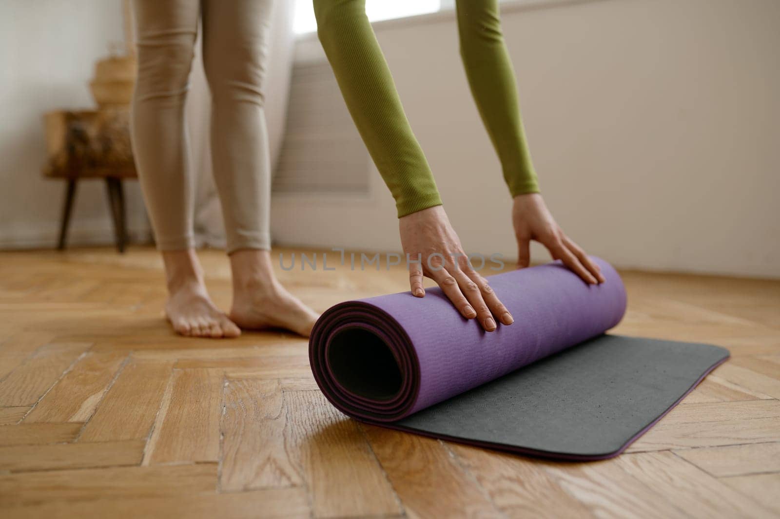 Closeup woman rolling yoga mat on wooden floor for morning meditation or active fitness practice