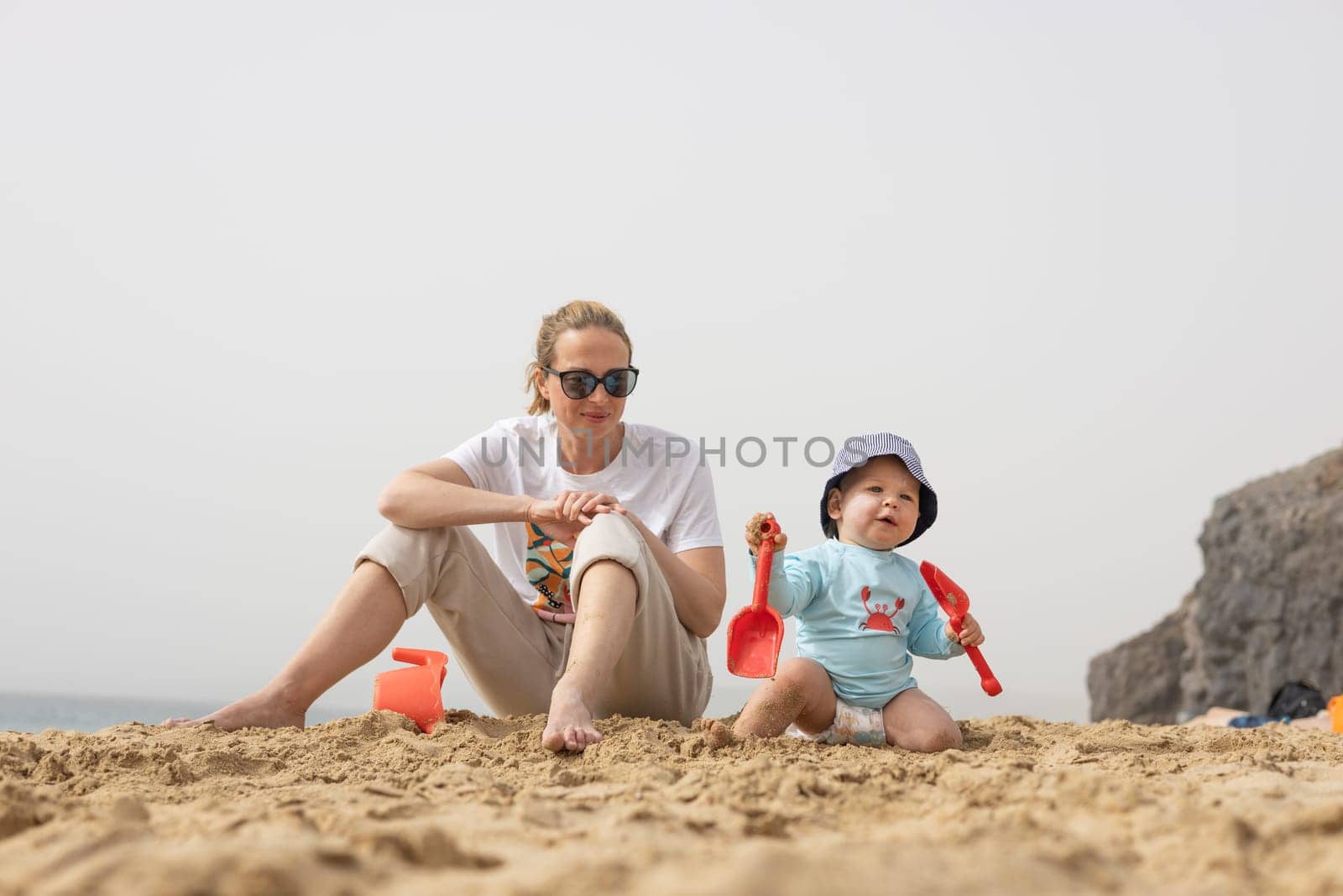 Mother playing his infant baby boy son on sandy beach enjoying summer vacationson on Lanzarote island, Spain. Family travel and vacations concept
