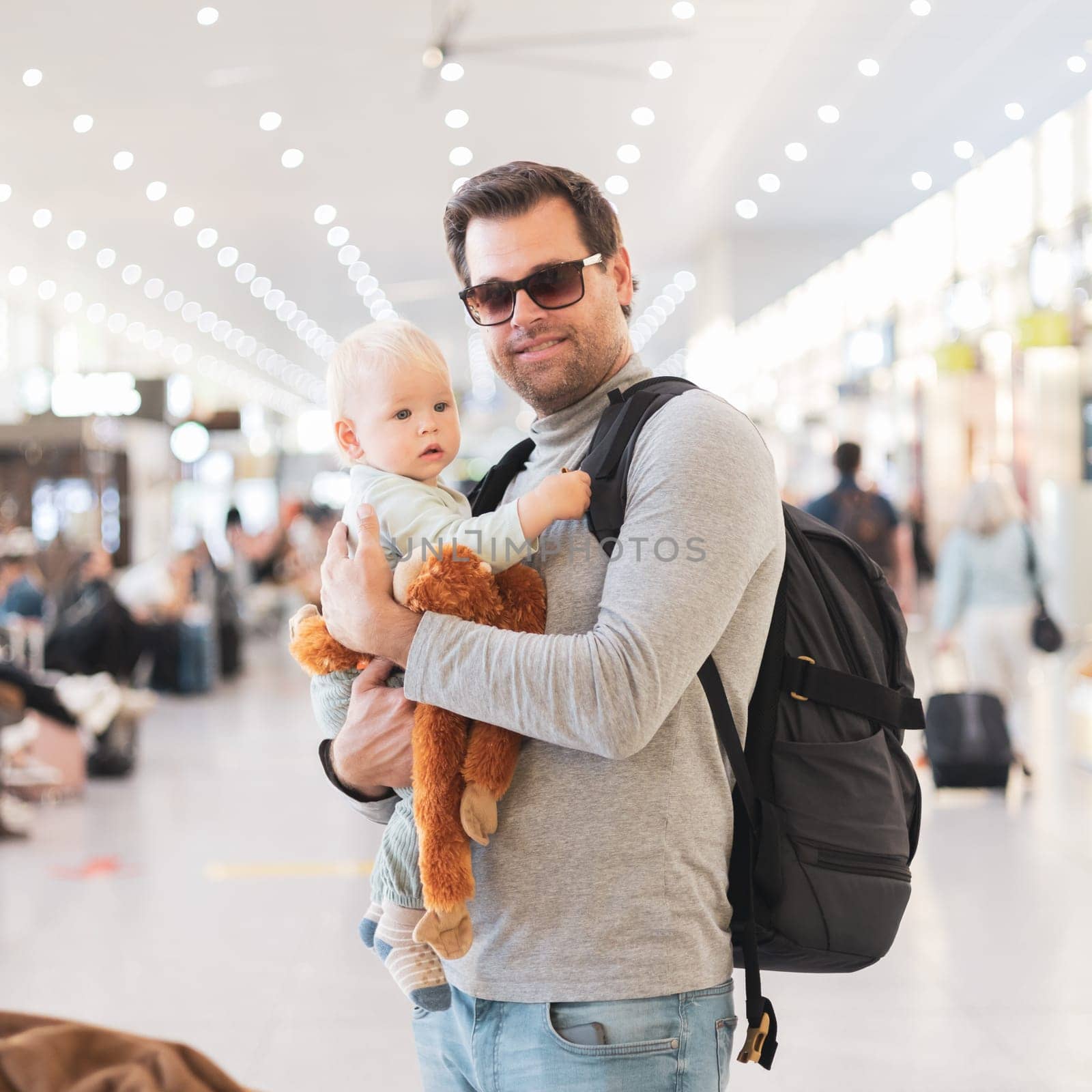 Father traveling with child, holding his infant baby boy at airport terminal waiting to board a plane. Travel with kids concept